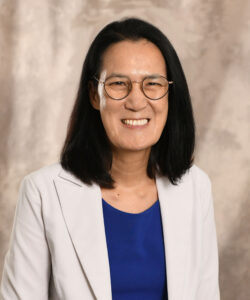 Eun-Jeon Hong, a Korean woman with shoulder-length dark hair and glasses, is smiling. She is wearing a navy blue top with a stone-colored blazer on top.